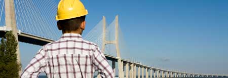 Engineer with yellow helmet looks at the bridge that goes over the water. With a link to the home page.